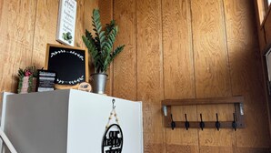 Una pared de madera con un letrero de bienvenida, una pizarra con un mensaje, una planta en maceta y un perchero.