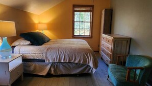 Une chambre à coucher avec un lit, une commode, une chaise et une fenêtre avec des stores.