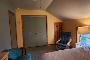 Een slaapkamer met een bed, een stoel, een bureau met een lamp, een kast en een raam.