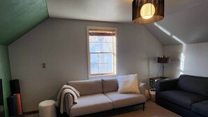 Une pièce de style loft avec un plafond haut, une grande fenêtre, un canapé beige, un canapé foncé et un lampadaire.
