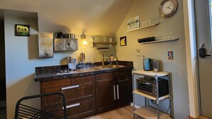 Une cuisine avec des meubles de rangement en bois foncé, une machine à café, une bouilloire et un grille-pain. Il y a une horloge au mur et une étagère avec des verres.