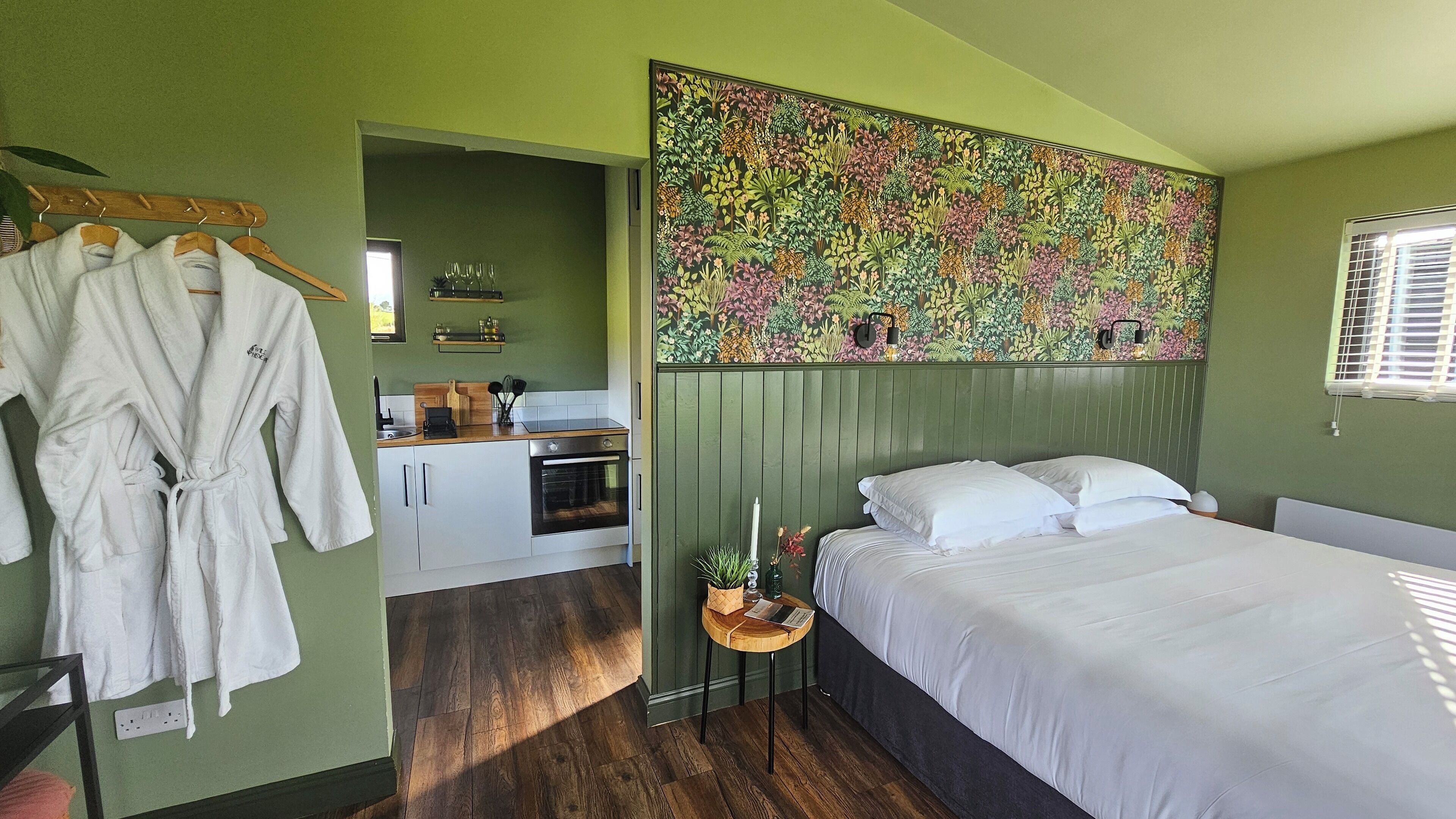 A bedroom with a bed, a nightstand, and a green wall with a floral mural.