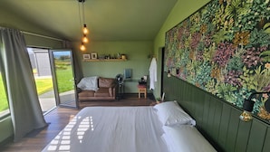 Un dormitorio con una cama grande, un escritorio con una computadora, una silla y vistas al exterior.