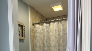 Een badkamer met toilet, een douchegordijn met bladmotief en een plafondlamp.