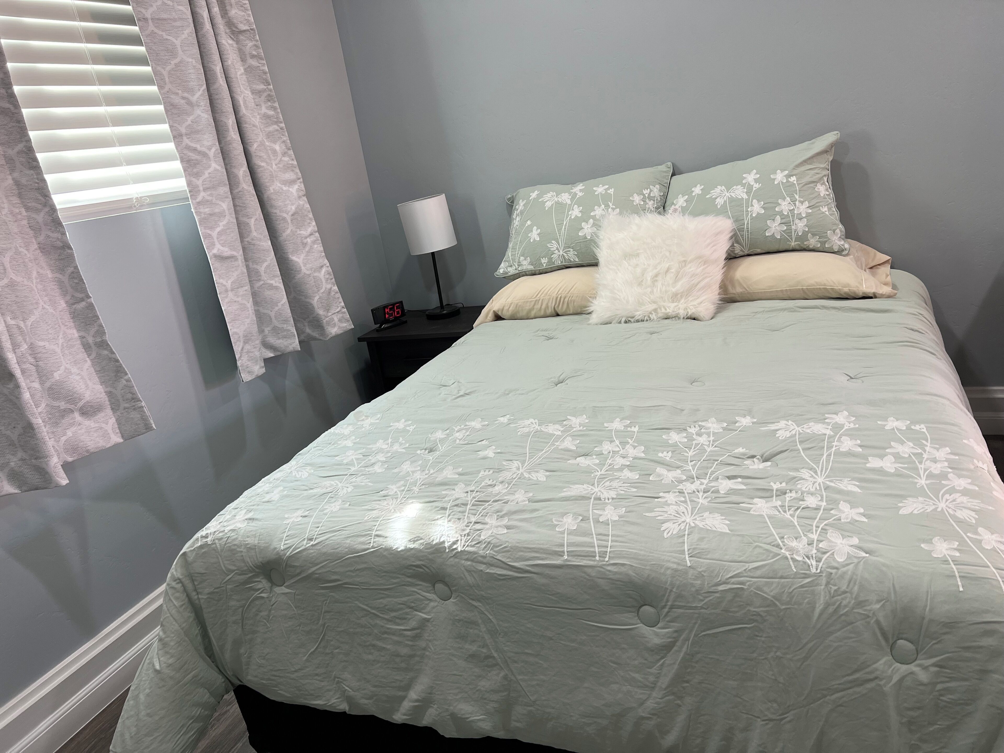 Een slaapkamer met een bed, nachtkastje, lamp en een raam met gordijnen.