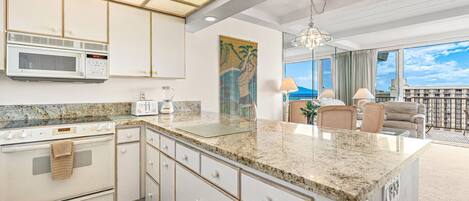 A modern kitchen with granite countertops, white cabinetry, a microwave, a toaster, and a stove.