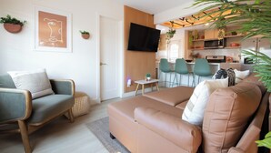 A modern living room with a sofa, a chair, a small table, and a flat-screen TV mounted on the wall.