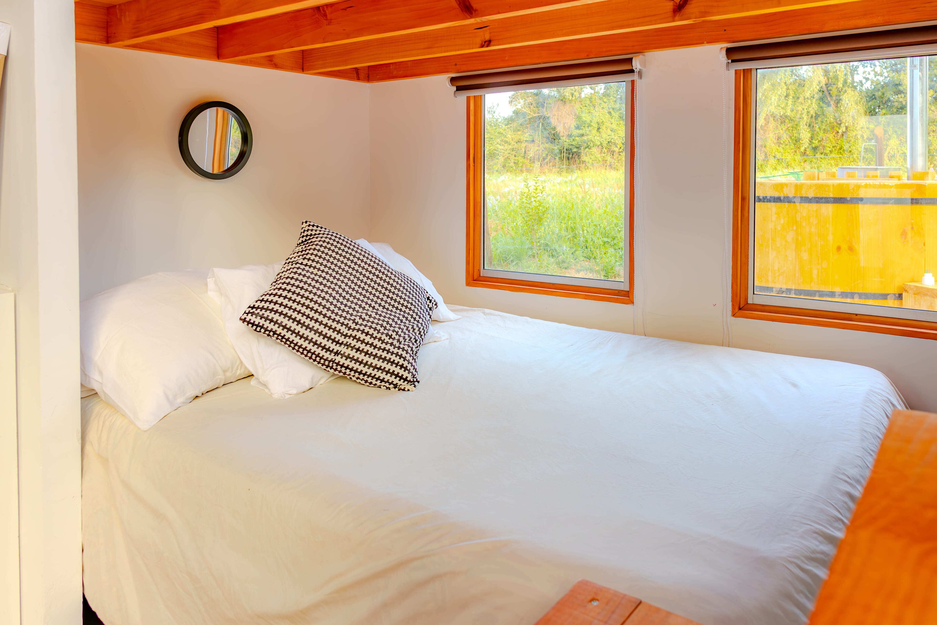 Un dormitorio con una cama, un espejo y dos ventanas.