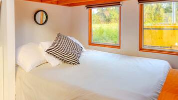 Un dormitorio con una cama, un espejo y dos ventanas.