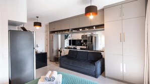 A modern hotel room with a bed, a sofa, a kitchenette, and a wardrobe.