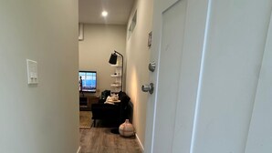 A hallway with a welcome mat, a door, and a TV in the background.