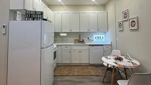 A compact kitchen with white cabinets, a built-in oven, and a refrigerator. There is a dining table with chairs and a rug on the floor.