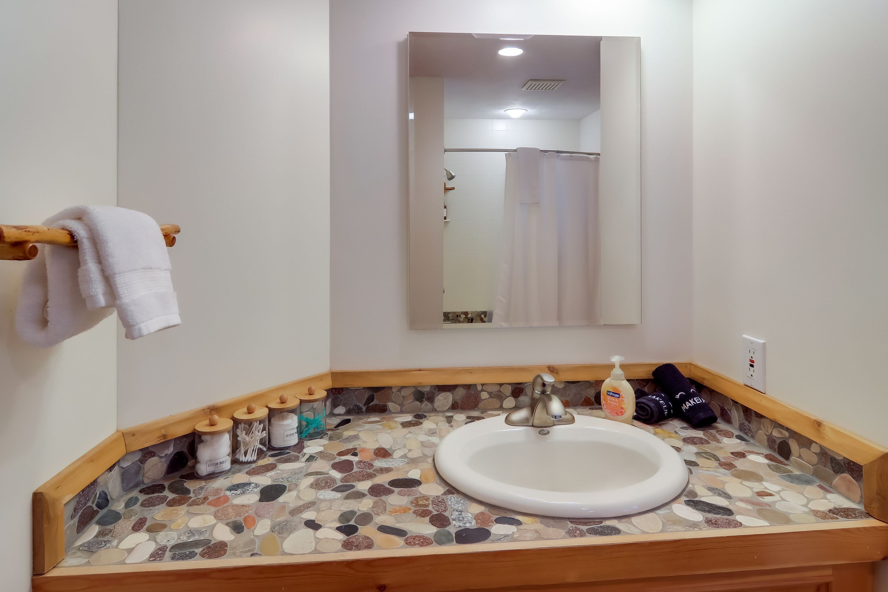 A bathroom with a stone mosaic countertop, a white sink, and a mirror above it.