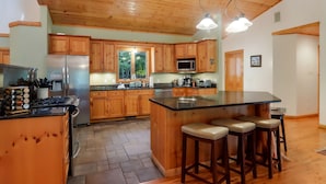 A spacious kitchen with wooden cabinets, a stainless steel refrigerator, a gas stove, and a large island with bar stools. - Boardman Monarch River HOT TUB Fireplace (Traverse City)