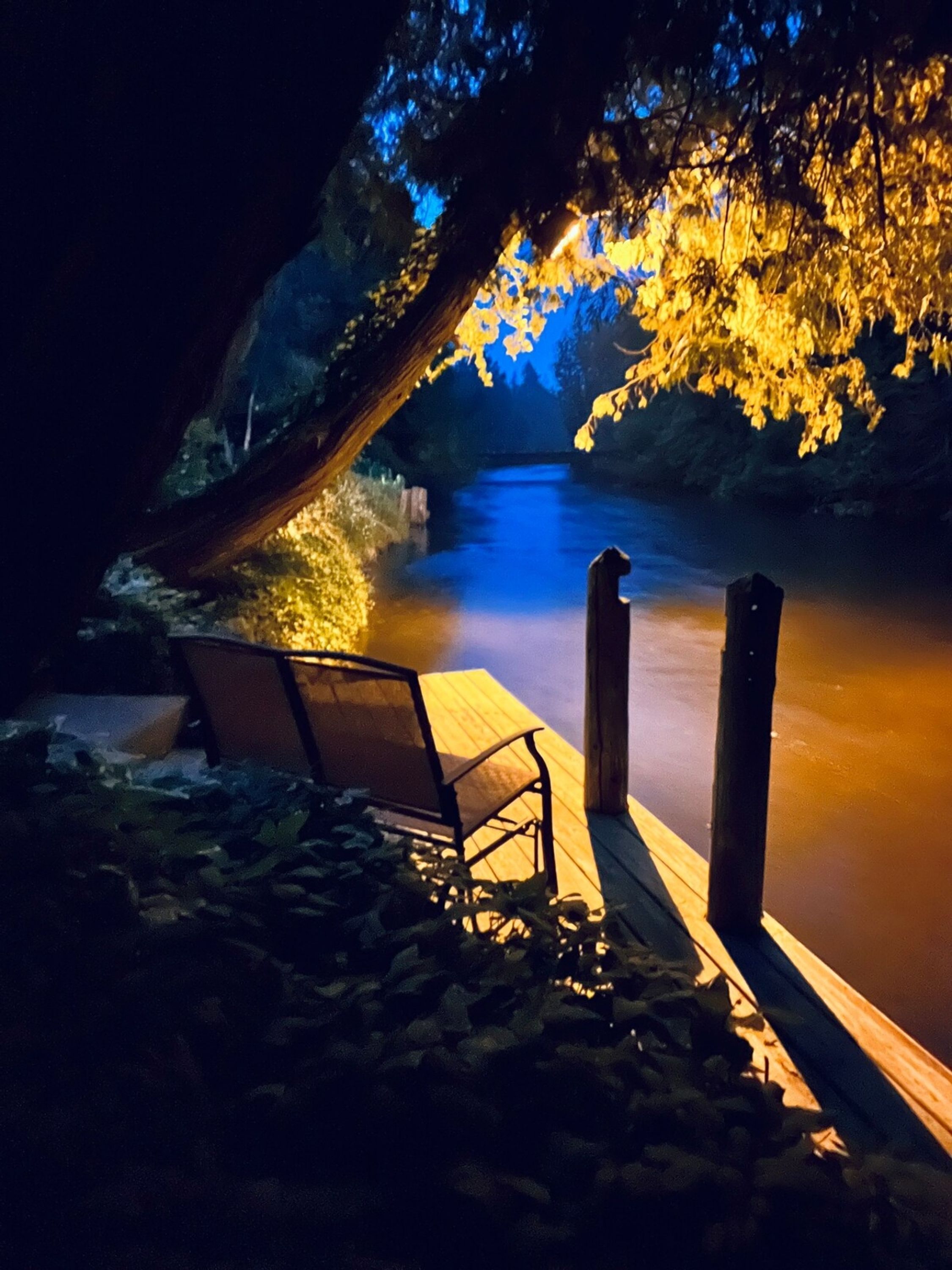 Une jetée en bois s’avançant dans une rivière la nuit, avec une chaise et une table à proximité.