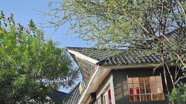 Um edifício tradicional com telhado inclinado, porta vermelha e janela com padrão quadriculado.