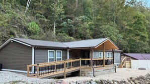 A cabin with a wooden deck and a porch, surrounded by trees. - The Wild & Wonderful – Steps from Hatfield-McCoy Trails (Matewan)