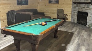 A pool table with balls, a sofa, a fireplace, and a ceiling fan in a room with wooden walls and flooring. - The Wild & Wonderful – Steps from Hatfield-McCoy Trails (Matewan)