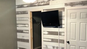 A bedroom with a bed, a TV mounted on the wall, a closet, and a door. - The Wild & Wonderful – Steps from Hatfield-McCoy Trails (Matewan)