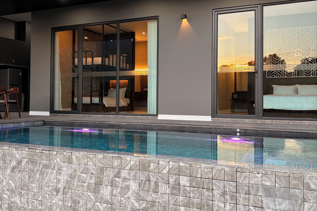 Ein moderner Poolbereich mit freiem Blick auf den Pool, einer steinverkleideten Kante und einer Glastür zu einem Raum mit Bett und Sonnenuntergangsblick.