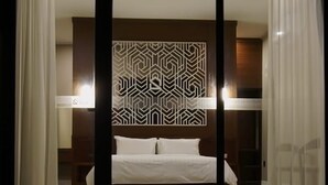 Habitació d'hotel moderna amb un llit gran, un panell de capçal amb un disseny geomètric i una taula de nit amb una làmpada.