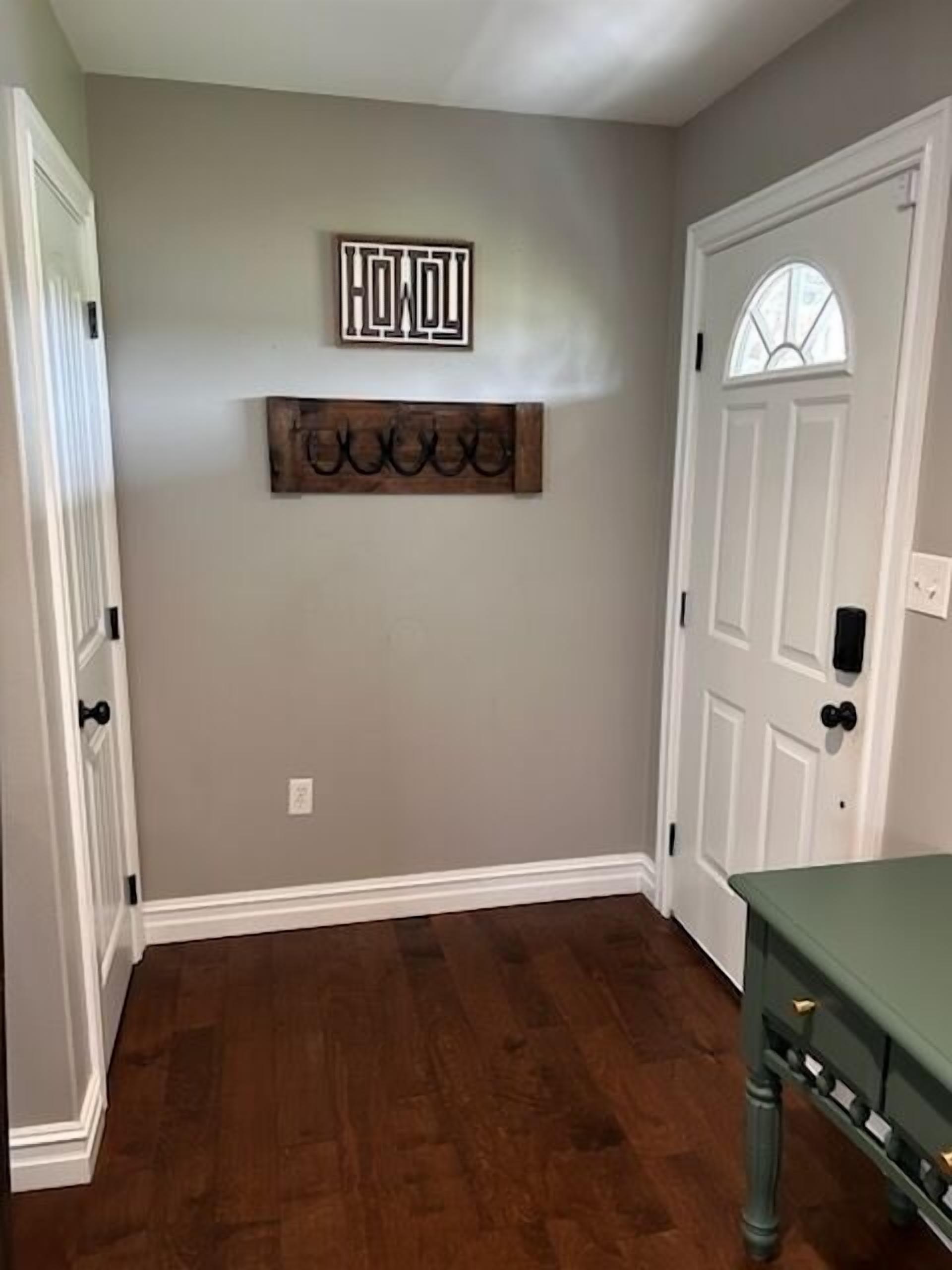 Un pasillo con piso de madera, una puerta blanca con ventana de vidrio y un cartel en la pared que dice 'HOW'.
