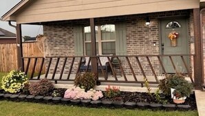 A single-story house with a front porch, brick exterior, and a small garden with various plants and flowers. - Adorable 2-bedroom house with AC in charming Pryor (Pryor)