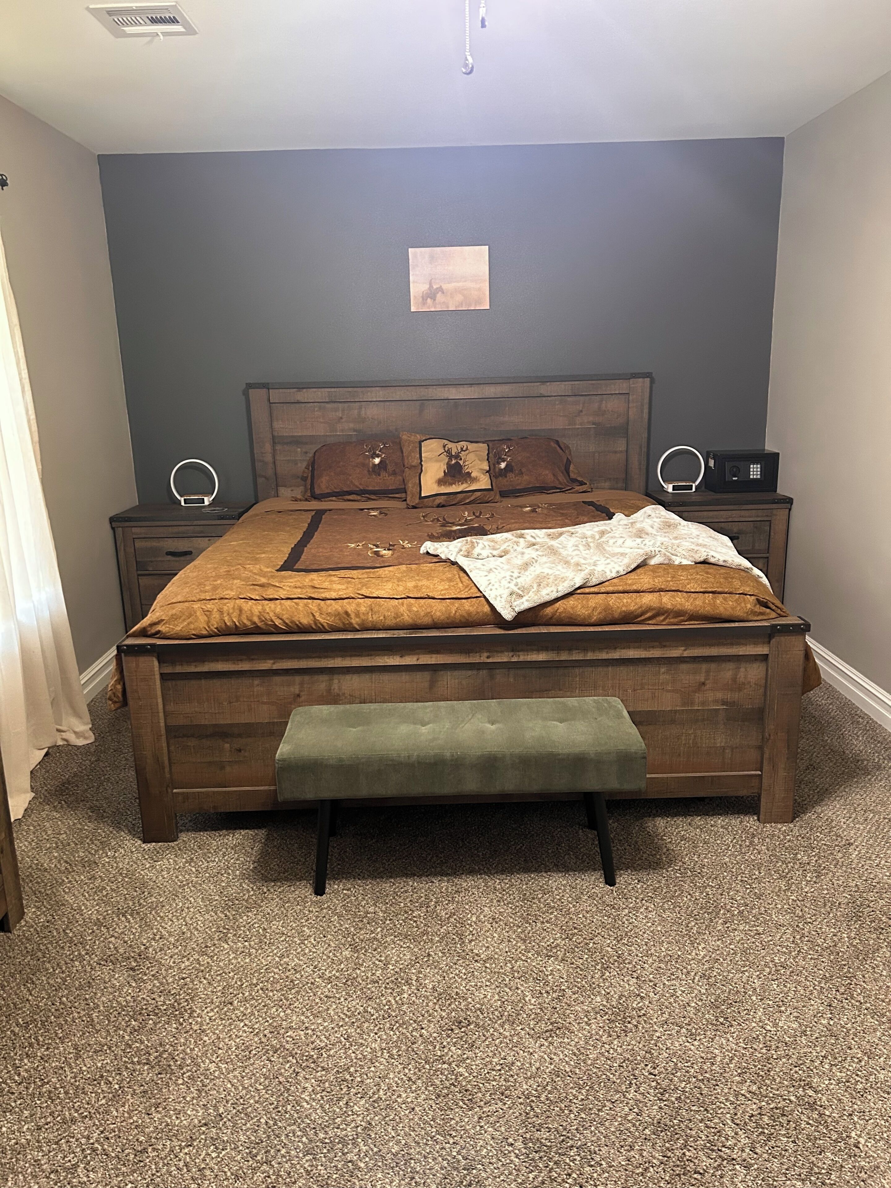 Een slaapkamer met een houten bed, een bankje, twee nachtkastjes met lampen en een klein decoratie aan de muur.