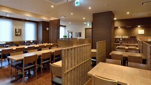Ein moderner Hotel-Speiseraum mit mehreren Tischen und Sitzgruppen, Holzwänden und einer Küche im Hintergrund.