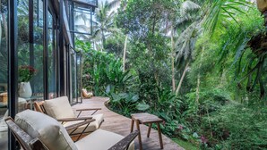 A lush garden with wooden deck seating and large windows overlooking dense foliage. - Twin House Ubud by Betterplace (Mas)