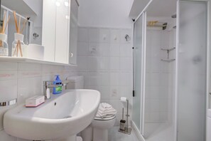 Un baño con lavamanos, inodoro y ducha blancos.