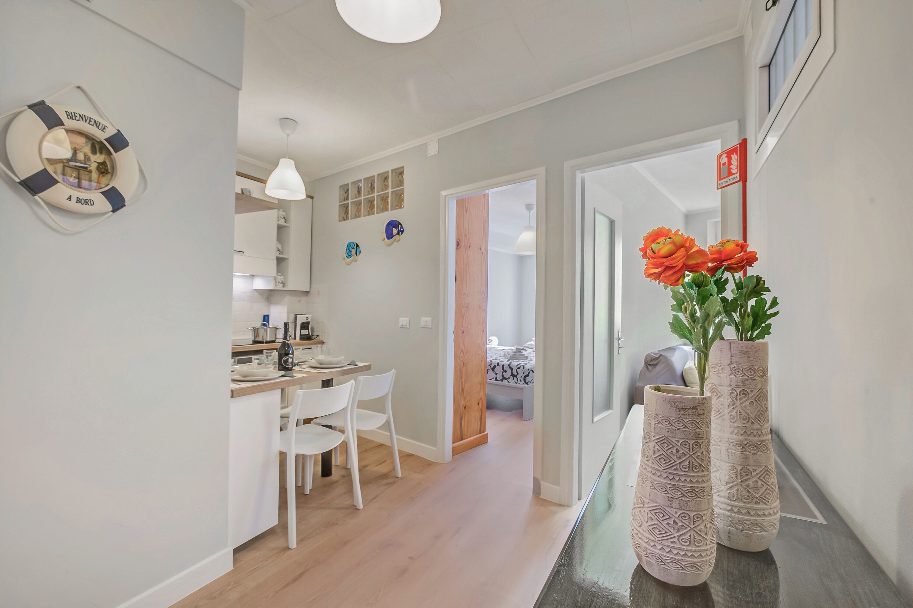 A modern kitchen with white cabinets, a dining area with white chairs, and a hallway leading to a bedroom.