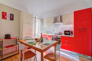 Una cocina moderna con armarios rojos, una mesa de comedor de madera dispuesta para dos personas y un microondas en la encimera.