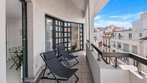 A balcony with two lounge chairs, a table with a chair, and a view of the cityscape. - Cannes Center - 5min from Croisette & Pal, Cannes, France (Cannes)