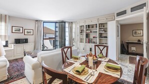 A dining area with a round table set for four, surrounded by white armchairs. A bookshelf filled with books and decorative items is visible in the background. - Cannes Center - 5min from Croisette & Pal, Cannes, France (Cannes)