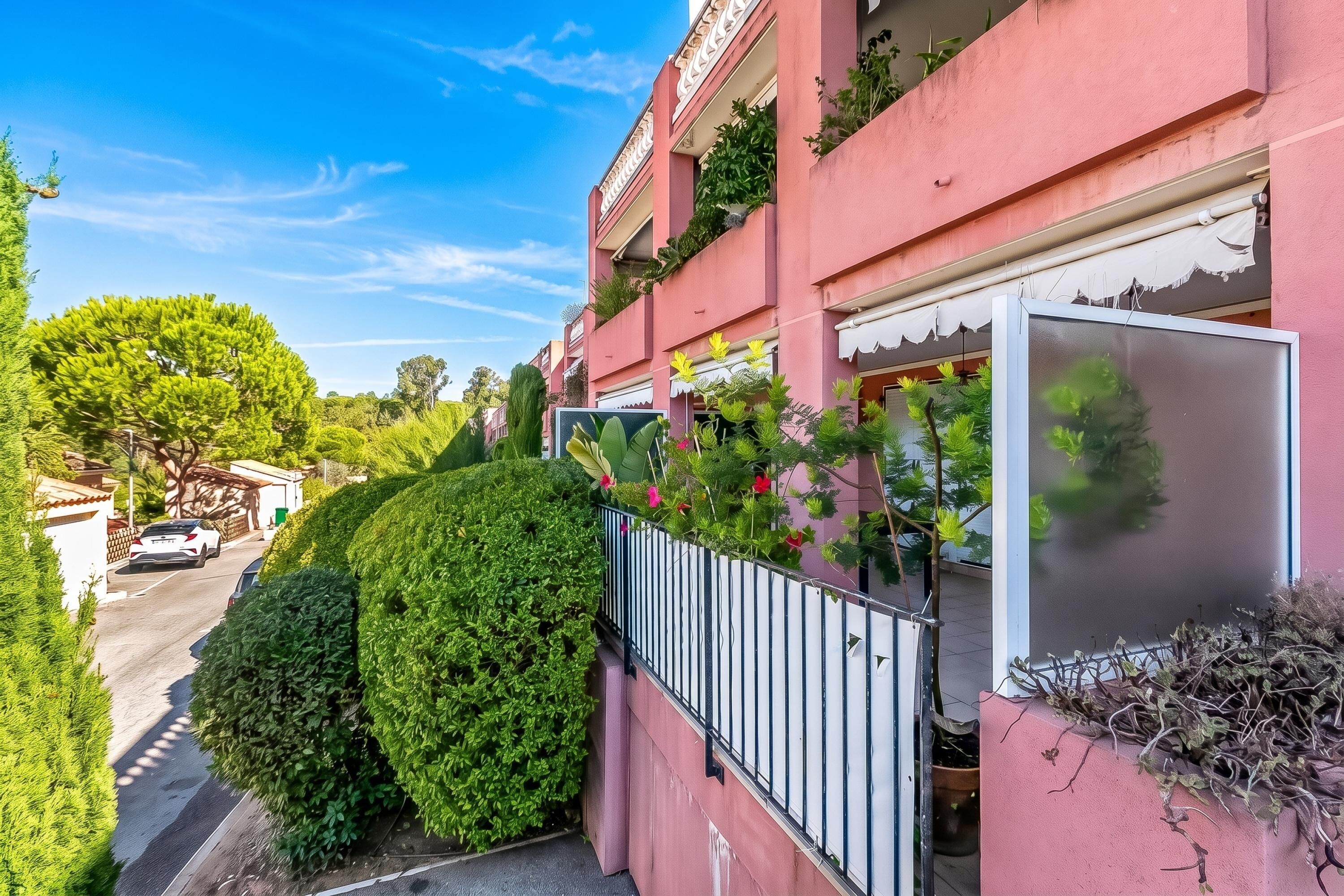 A residential building with a pink facade, a balcony with plants, and a clear sky.