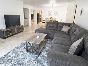Una sala moderna con un sofá gris, una mesa de centro y un televisor sobre un mueble de madera.
