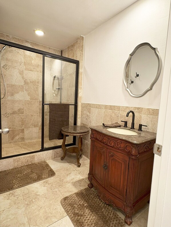 Un baño con cabina de ducha acristalada, tocador con lavabo y espejo en la pared.