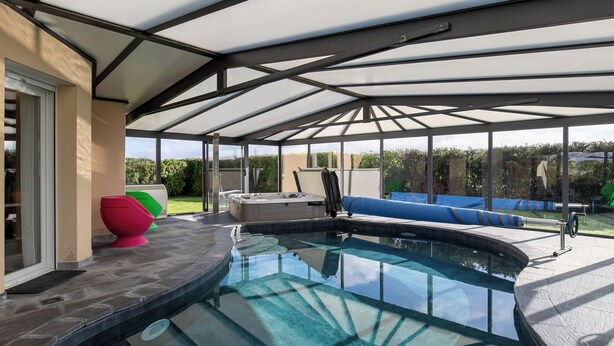 A covered outdoor swimming pool with a hot tub, seating area, and a view of the surrounding garden. - Chez David by Interhome (Kersaint-Plabennec)