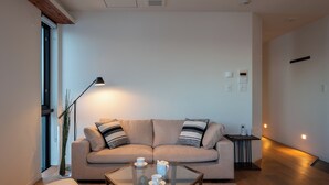 A modern living room with a beige sofa, a glass coffee table, and a floor lamp. - Yotei Dream One (Kutchan)