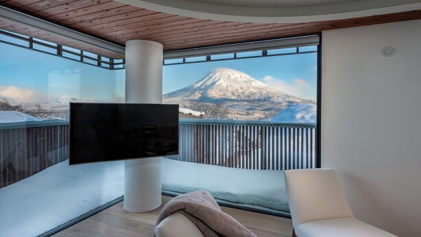 A modern room with a large flat-screen TV, a comfortable chair, and a view of a snow-capped mountain. - Yotei Dream One (Kutchan)