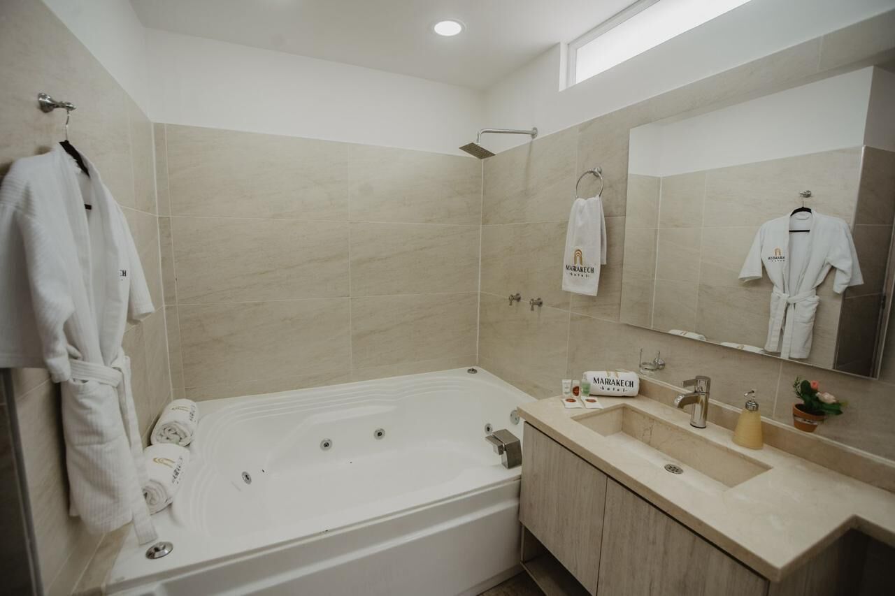 A modern bathroom with a large bathtub, a sink, and a mirror. There are towels and a sign on the wall.