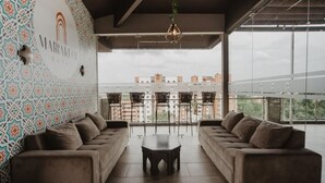 A modern hotel lobby with patterned walls, two sofas, a central table, and a view of buildings through large windows. - Noma Hotel And Rooftop (Cali)