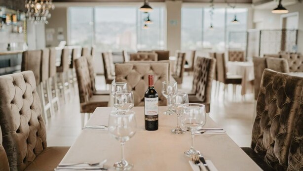 A dining area with a long table set for a meal, featuring a bottle of wine, multiple wine glasses, and neatly arranged cutlery. - Noma Hotel And Rooftop (Cali)