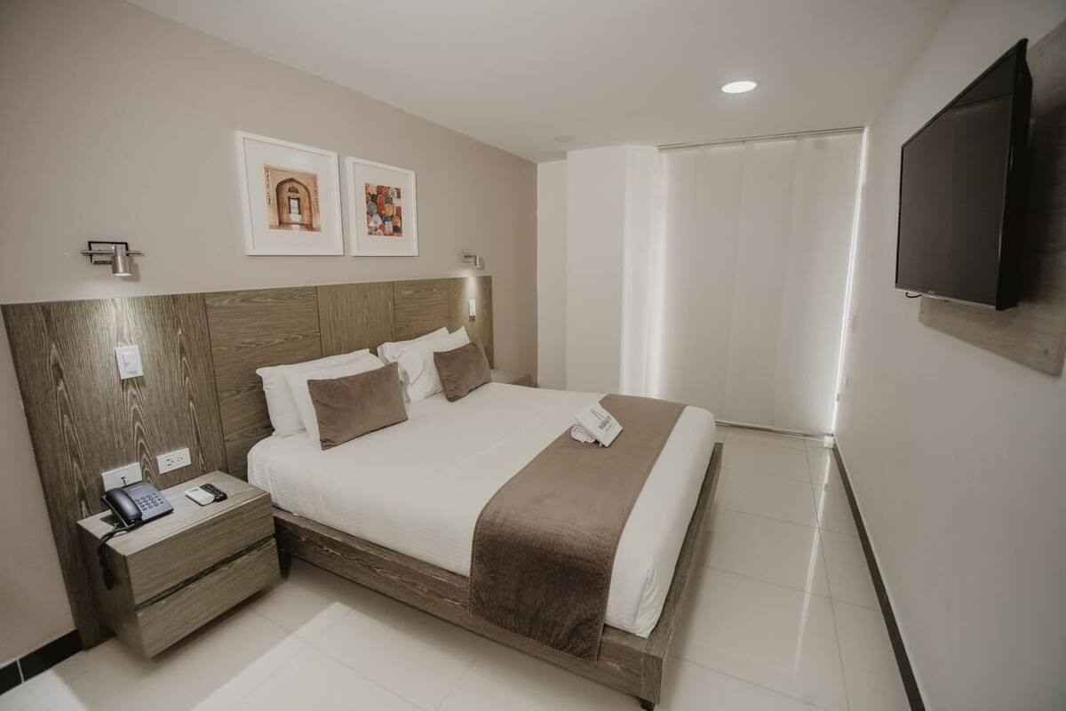 A modern hotel room with a wooden headboard, a flat-screen TV, a bedside table with a phone, and artwork on the wall.