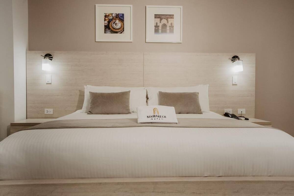 A hotel room with a large bed, two wall-mounted lights, and a pillow with the hotel name.