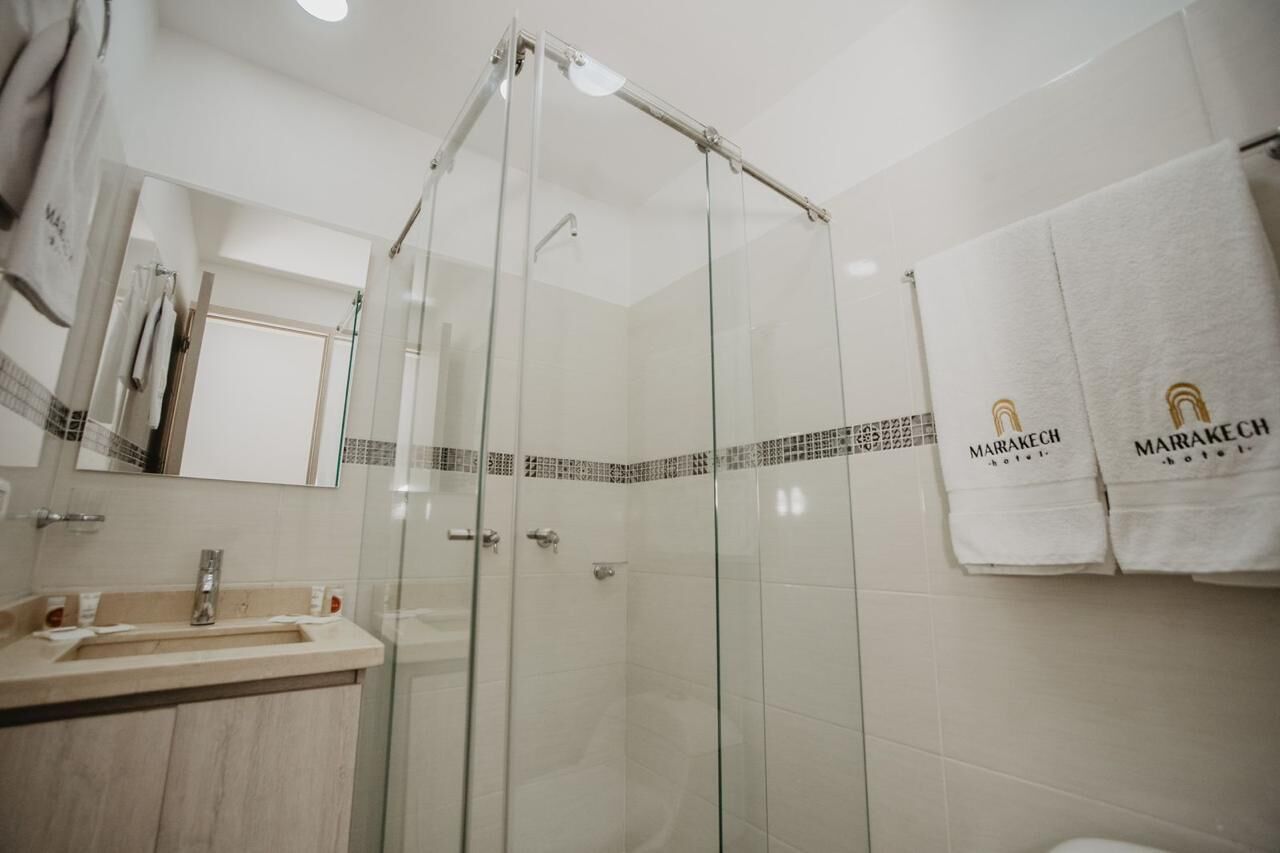 Un baño moderno con ducha envuelta en vidrio, lavamanos con espejo y perchero con toallas de marca.