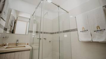 Un baño moderno con ducha envuelta en vidrio, lavamanos con espejo y perchero con toallas de marca.