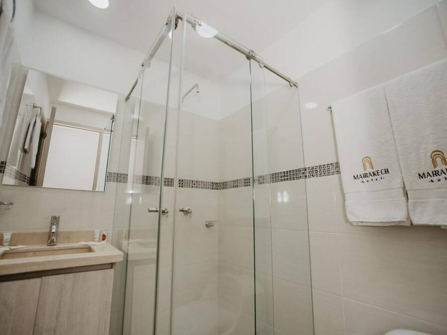 Un baño moderno con ducha envuelta en vidrio, lavamanos con espejo y perchero con toallas de marca.