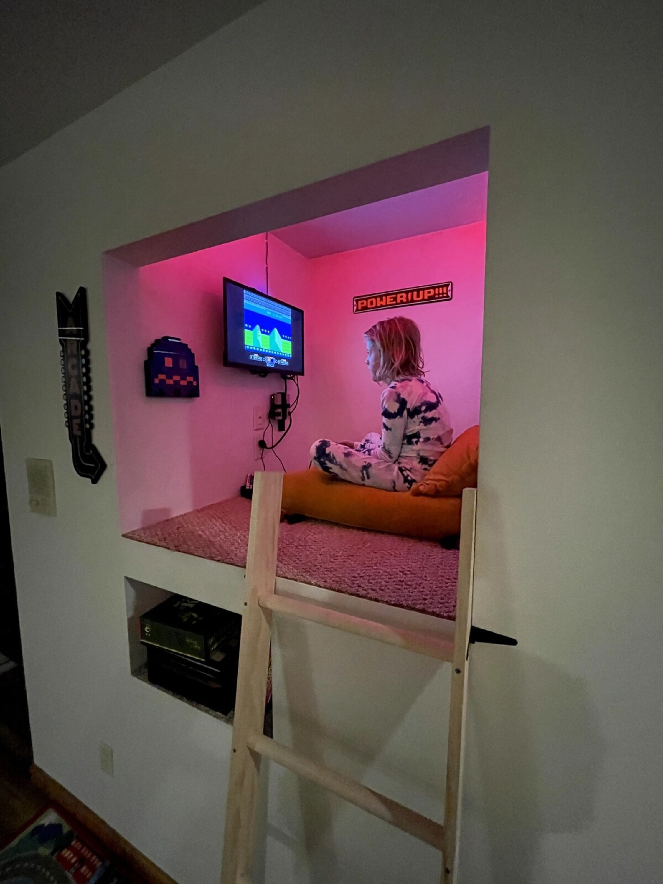 A room with a bunk bed, a television mounted on the wall, and a neon sign.